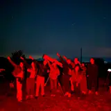 Participants at a nighttime star party using a telescope under red-light conditions